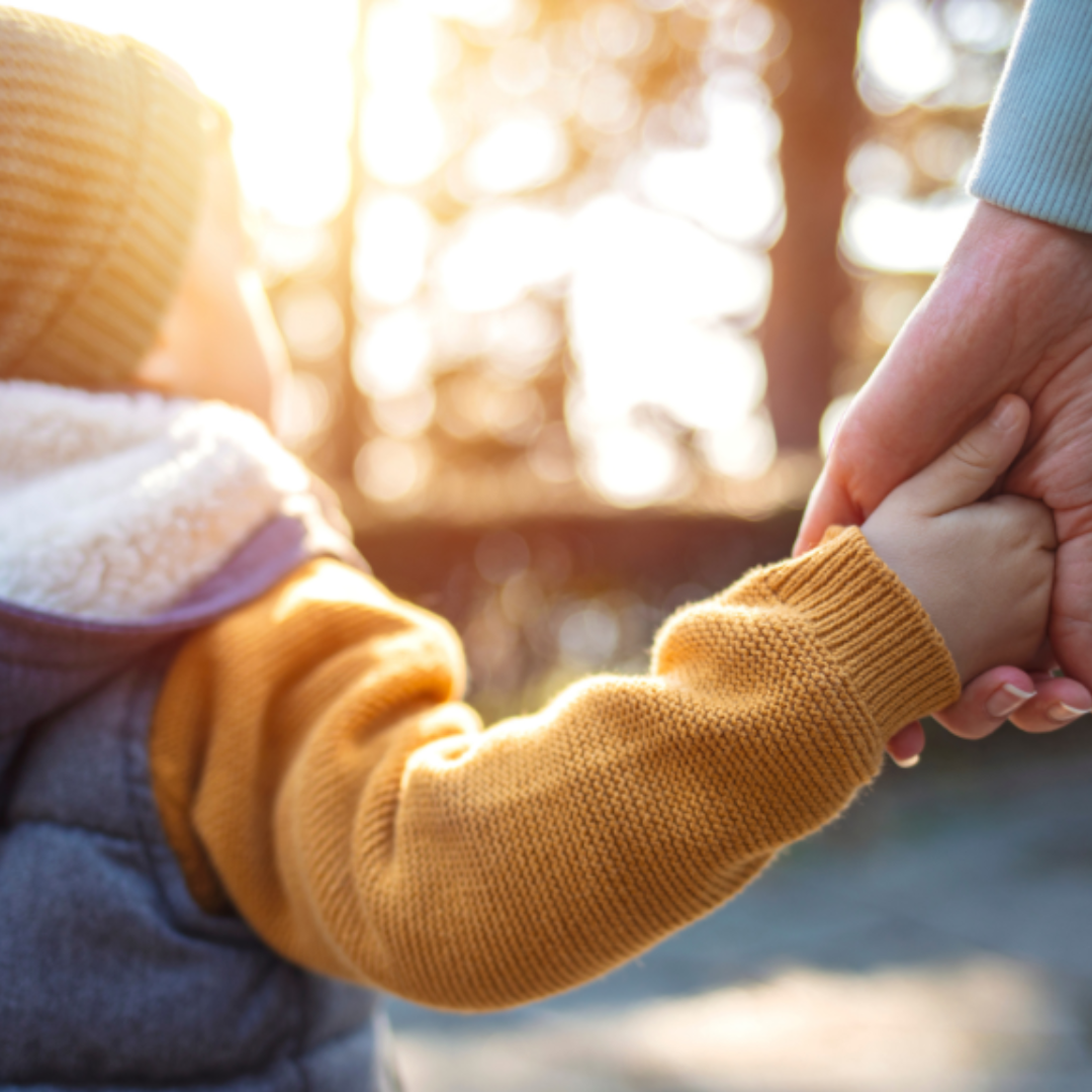 close up of a young kid holding an adult hand and walking outside in the winter