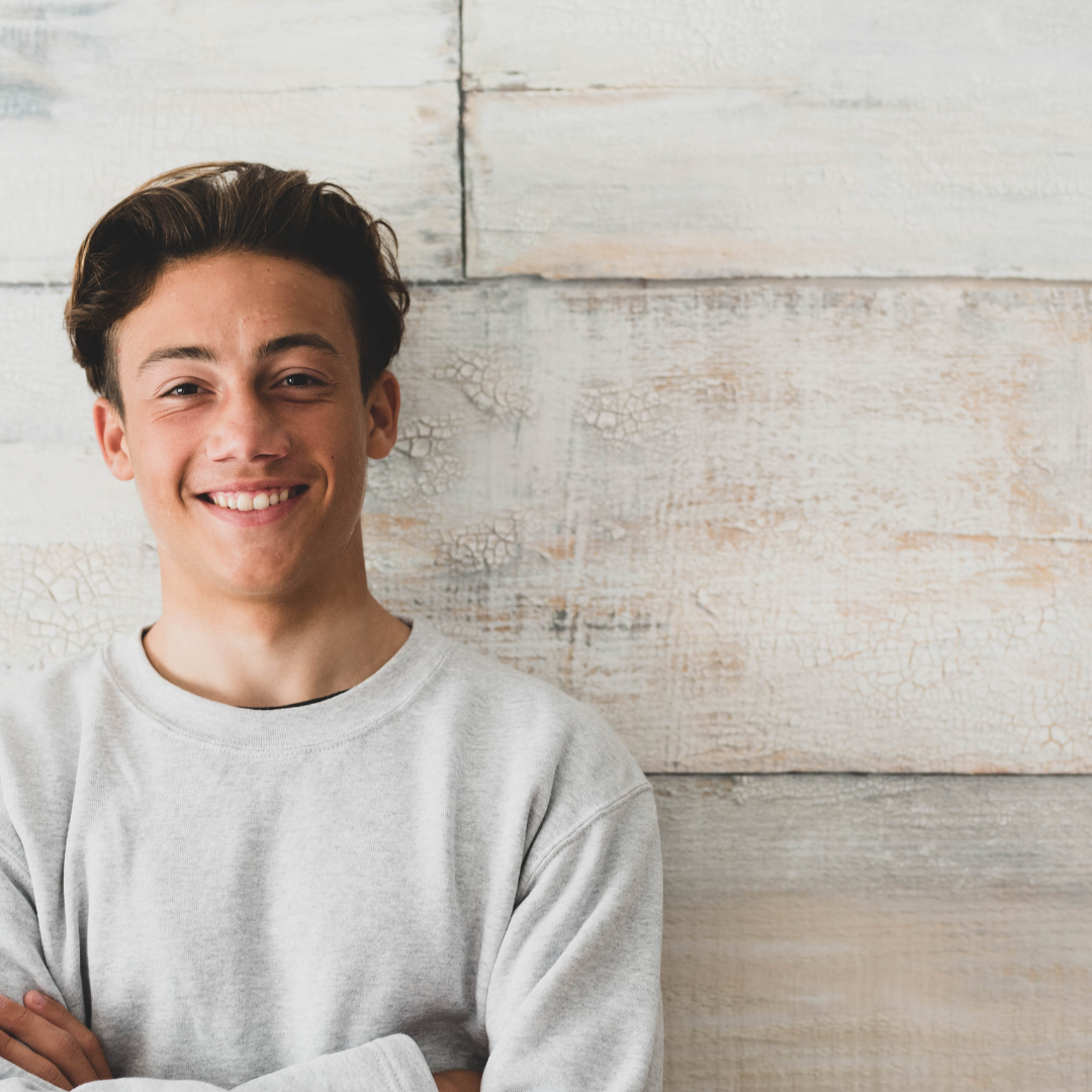 A young person smiling and standing in front of a wall