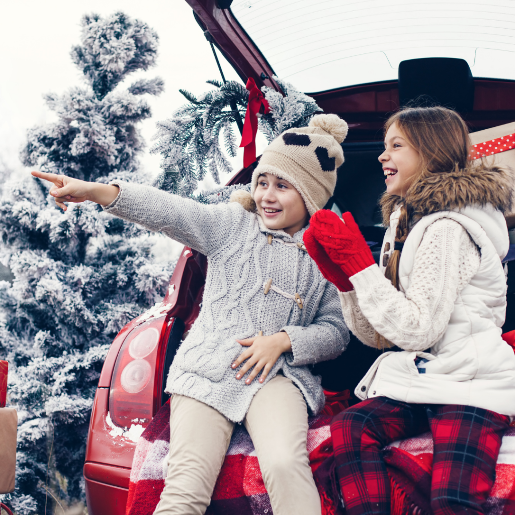 Photo of two kids sitting in the trunk of a car filled with gifts