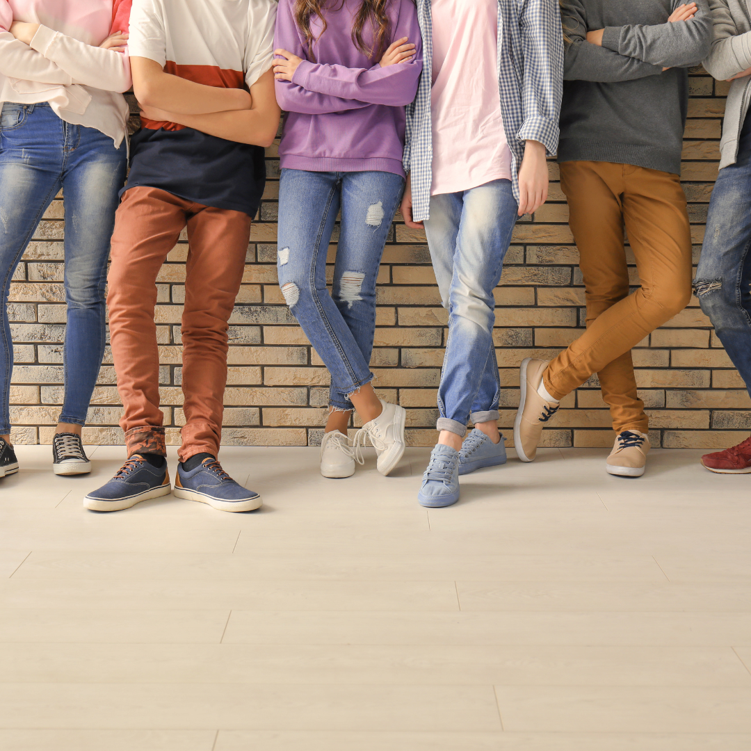 a group of teenagers leaning against a wall. the photo only shows their legs and feet