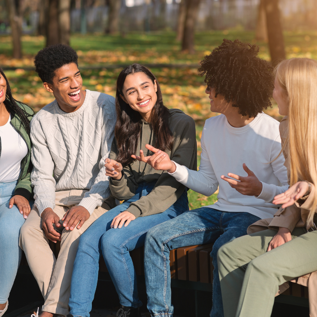 A group of teenagers sitting on a bench in a park, talking and laughing